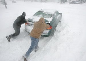 people pushing a car stuck in the snow