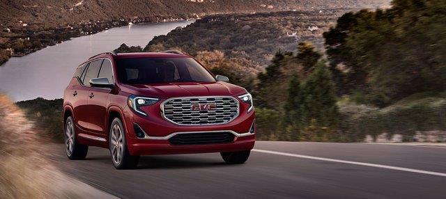 2018 red GMC Terrain driving on a hilly highway overlooking a river valley