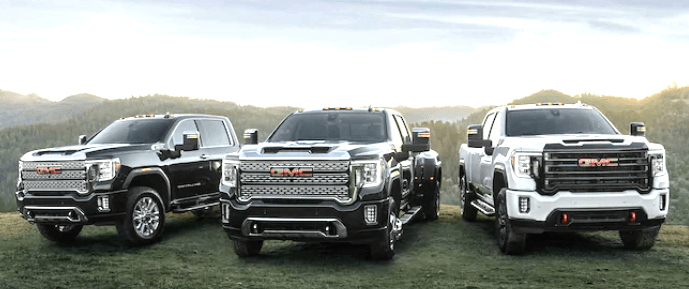 Three GMC Sierra HD's parked next to eachother on a grassy hilltop